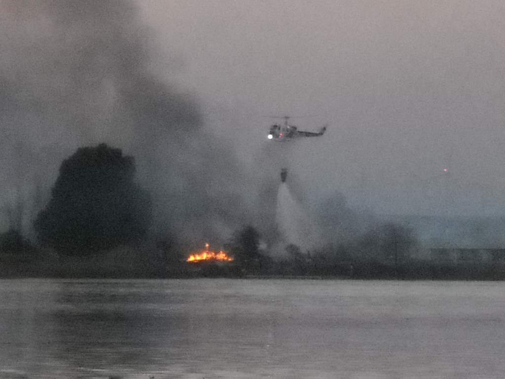 A helicopter attempts to douse the final flames on Kimball Island, during the fire, today. By Allen Payton