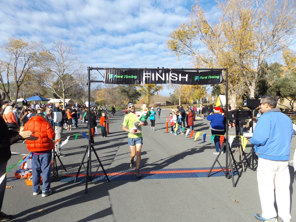 Overall 10K Run winner Brian Mohrlant crosses the finish line after picking up his daughter near the end of the race.