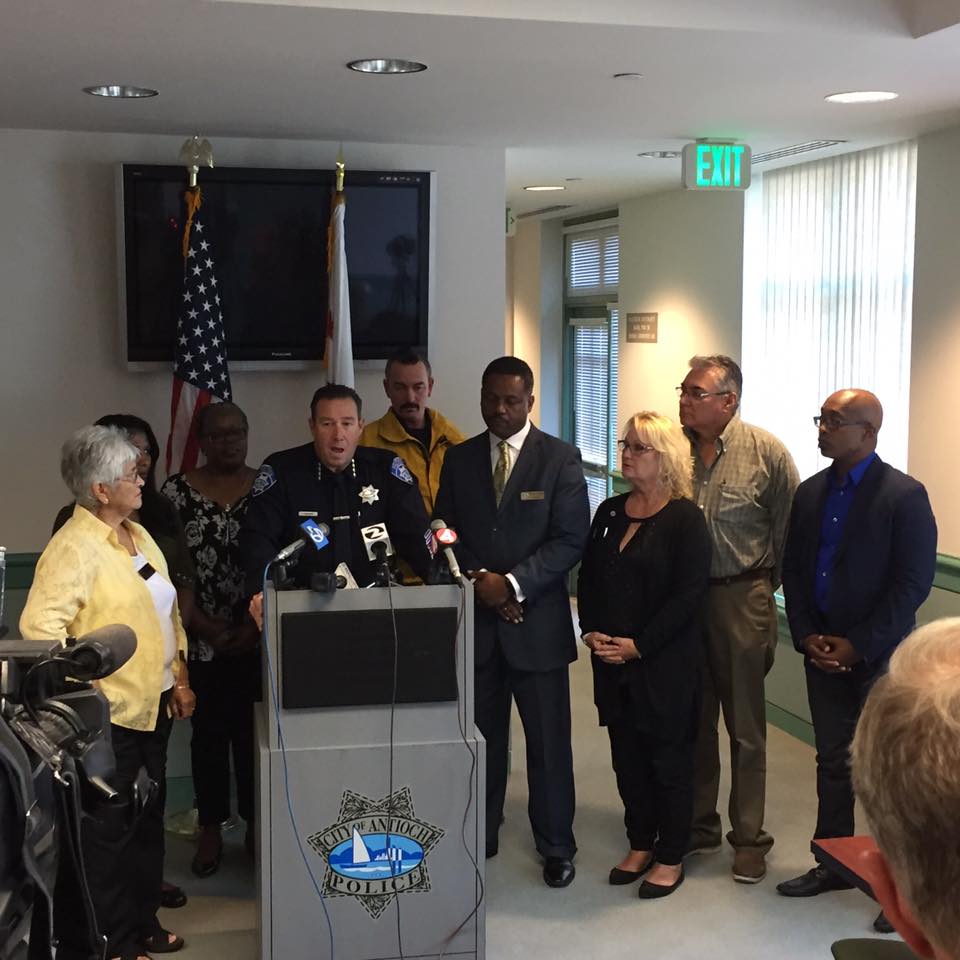 Antioch Police Chief Allan Cantando is joined by Antioch Mayor Wade Harper, (in suit, right), all four council members and others, as he announces the arrest of two suspects in last Wednesday's hate crime, at a press conference Tuesday afternoon.